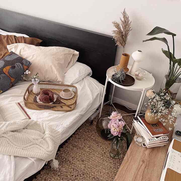 Natural color and beige-white toned bedroom featuring a rattan rug, side table with vases, and knit throw creating a cozy atmosphere
