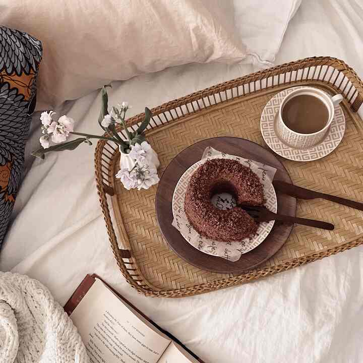 Natural beige-toned bedroom featuring a rattan tray with coffee and donut, linen bedding and knit throw creating a cozy home cafe atmosphere