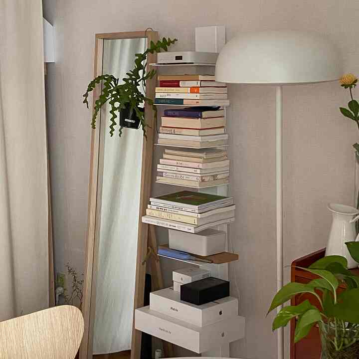 ナチュラルな色調のワンルームリビング、本棚や全身鏡、フロアランプ、植物が配置されたシンプルで落ち着いた雰囲気の空間