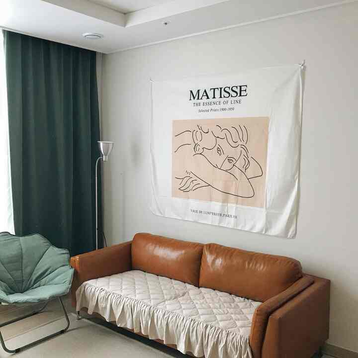 ナチュラルな色調のリビング、茶色のレザーソファと緑色のアームチェア、壁にマティスのポスターが掛けられた印象的な空間