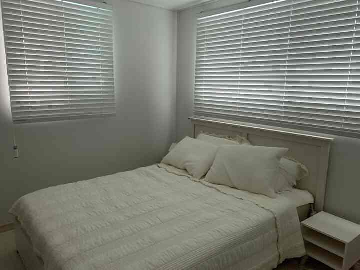 Cozy 2-person bedroom with warm cream white and wood tones, featuring clean wood-form blinds and soft bedding