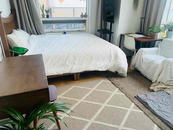 Natural bedroom with white bedding and wood tone furniture, featuring large windows and a cozy rug
