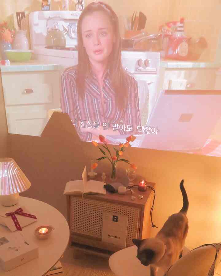 暖かいベージュとナチュラルな木目調のリビング、円形テーブルとナイトテーブルにキャンドルや造花、テーブルランプが配置された雰囲気のあるホームシネマ空間