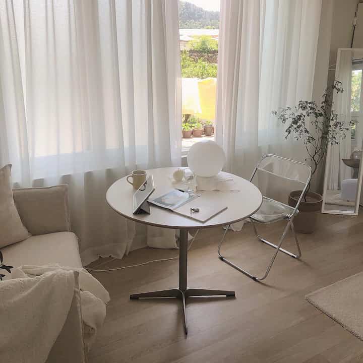 Cozy bedroom space in warm ivory and white tones featuring single sofa, round table, natural light and indoor plant accent