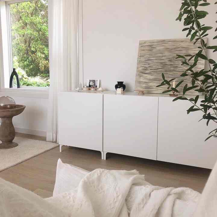 Bright living room with white and wood tones, featuring a BES TA storage cabinet centrally placed, natural light and plants for a natural modern feel