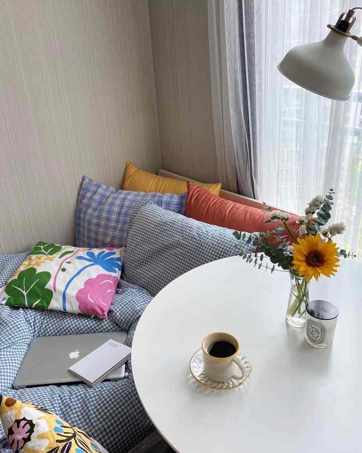 White and blue toned small room home cafe space featuring round table with vase and coffee cup, cozy cushions creating a warm atmosphere