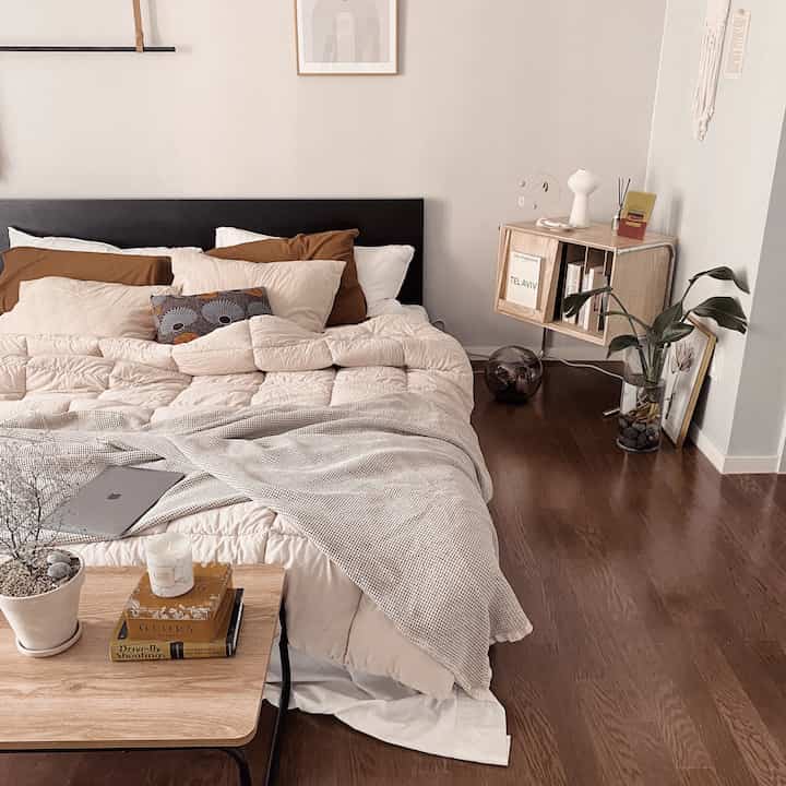 Beige and wood tone bedroom featuring a cozy bed, nightstand with vase and mobile, creating a simple and natural atmosphere