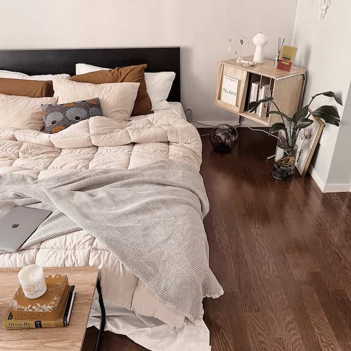 Natural modern bedroom in beige and wood tones, featuring cozy bedding and a wooden magazine rack for a calm atmosphere