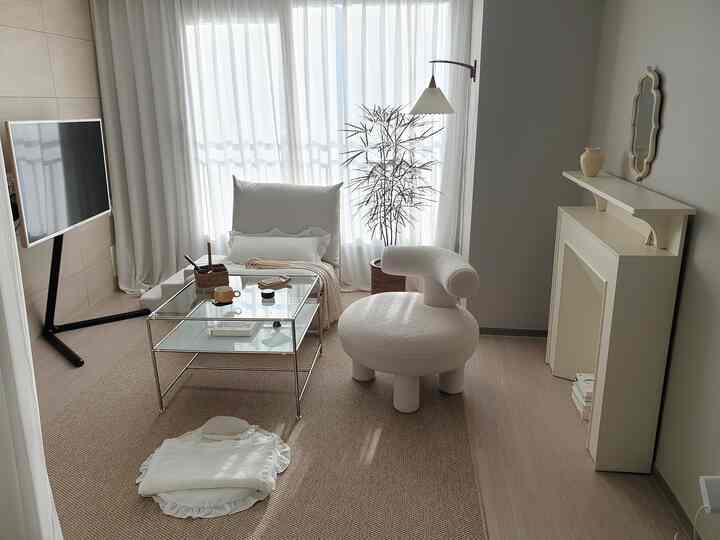 Bright white and beige-toned living room featuring a round armchair and glass coffee table in a natural atmosphere