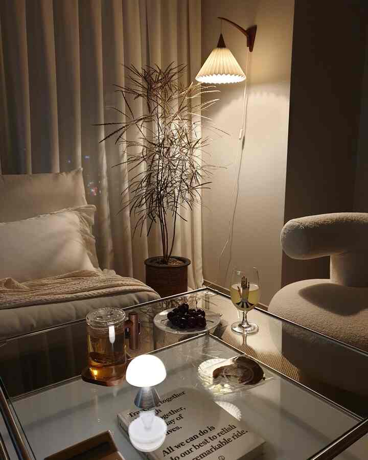 暖かいベージュ調とナチュラルな雰囲気のリビング、ソファとアームチェア、テーブル上にミニライトと植物が配置された落ち着いた空間