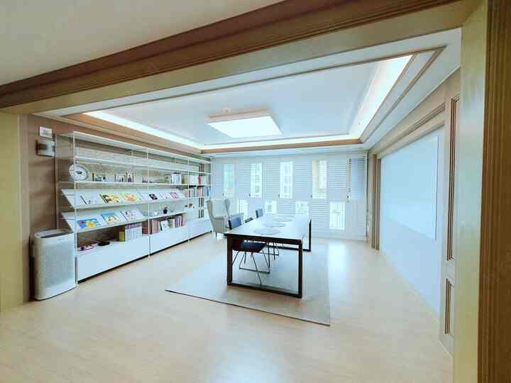 Bright and comfortable study and reading space in white and beige tones, featuring a large bookshelf and long table