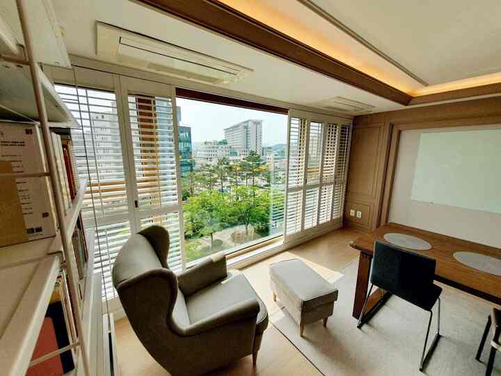 Natural modern living room featuring wood tone dining table, Strandmon armchair, and large window with louver shutters, bright and cozy space