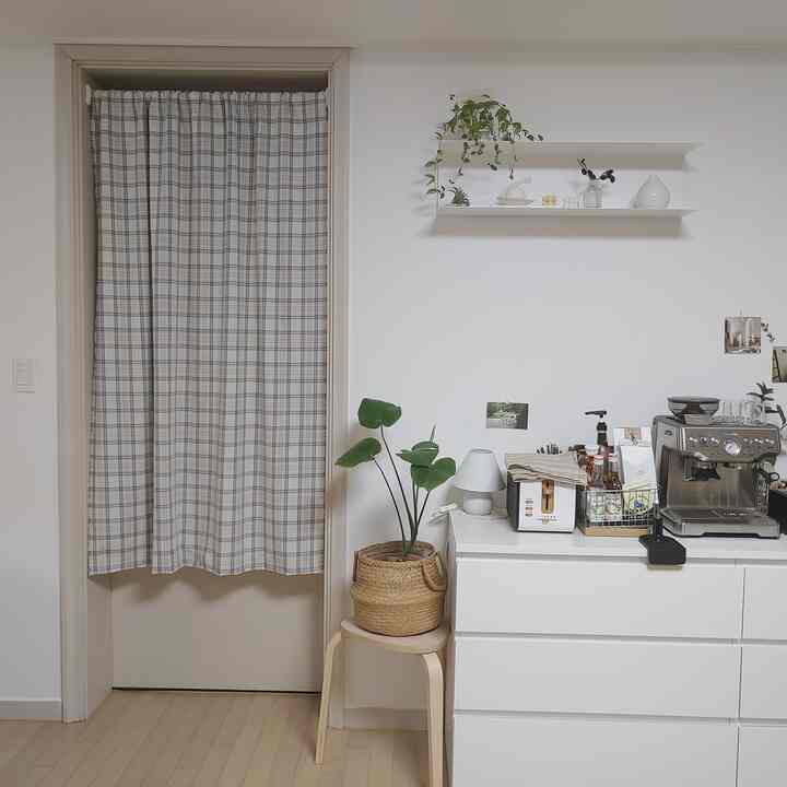 Natural-toned home cafe space with white walls and drawers, featuring a coffee machine and plants in a clean interior