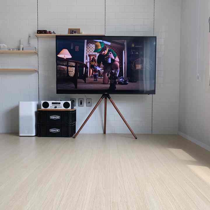 Modern living room with white walls and wood tone floor featuring a tripod TV stand and air purifier in a clean setup