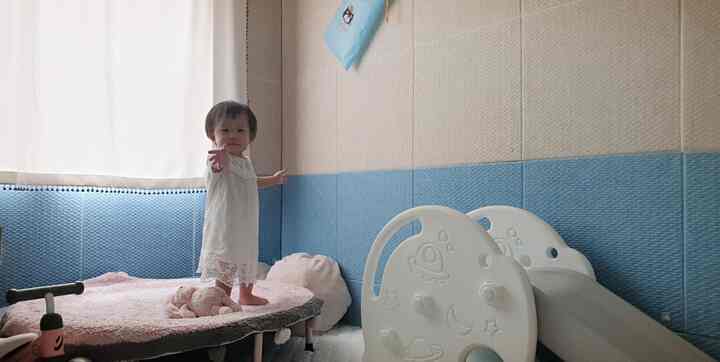 A white and blue toned baby room featuring a trampoline and slide in a safe, cushioned play area