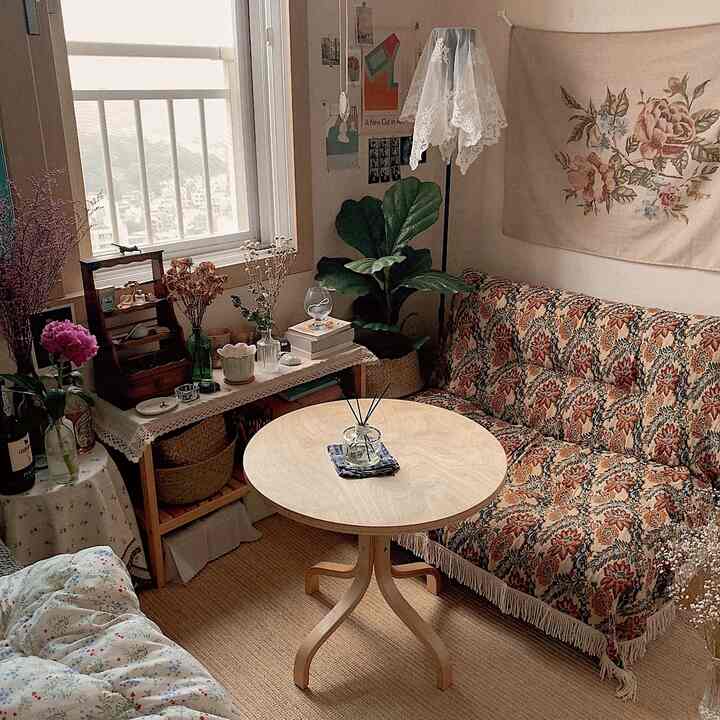 ナチュラルな色調のヴィンテージ風小部屋、花柄のソファと丸いテーブルが配置された居心地の良いインテリア