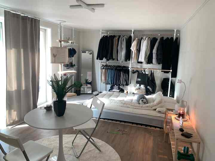 White and brown toned studio apartment bedroom featuring clothing rack and storage ideas in a simple modern space