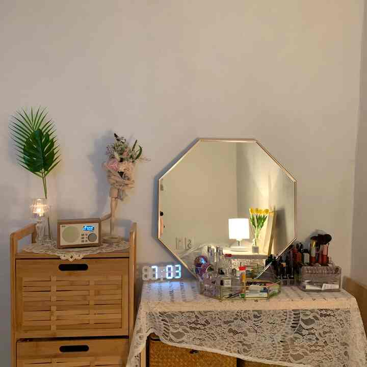 White walls and natural tone furniture in a bedroom vanity area featuring a vase and LED clock, creating a cozy atmosphere