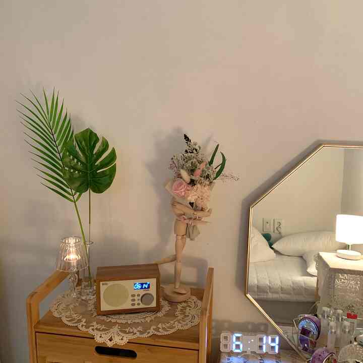 ナチュラルな色調の寝室、木製家具と花瓶が置かれたテーブルに時計と照明が調和した雰囲気のあるインテリア