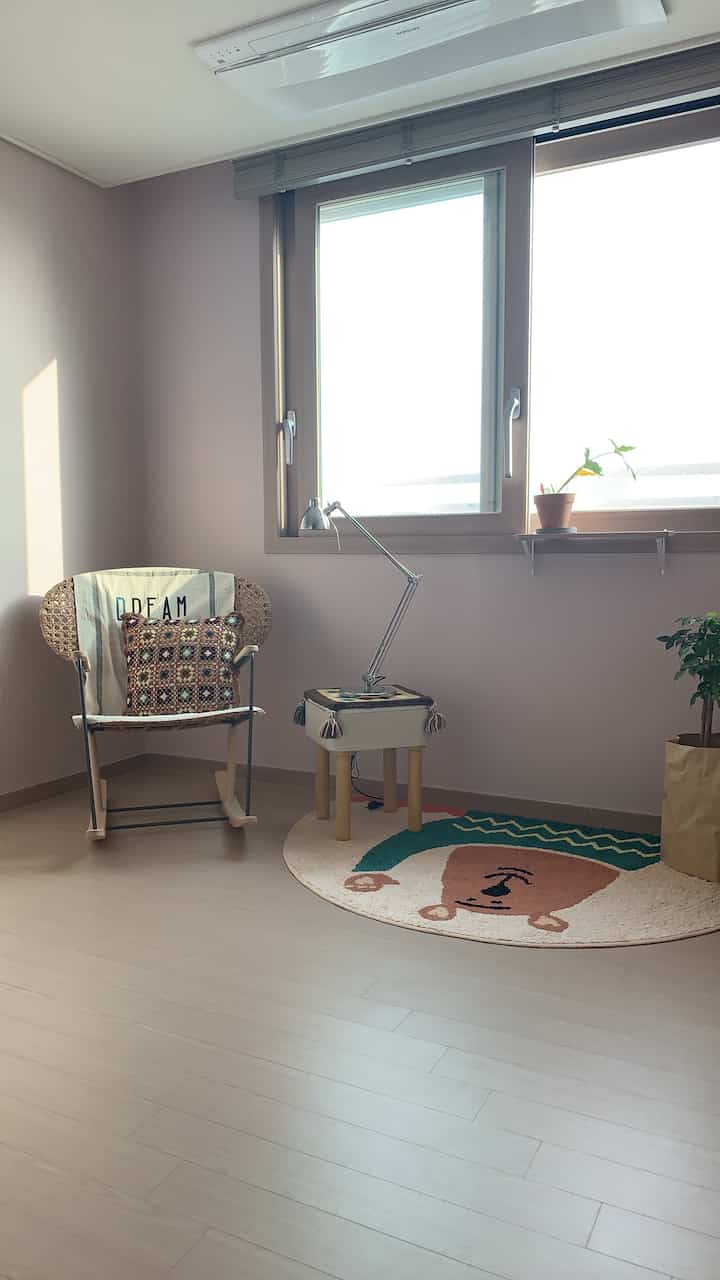 暖かいライトブラウンの木目調の子供部屋、ラタンのアームチェアとかわいいキャラクターラグが配置されたナチュラルな雰囲気の空間