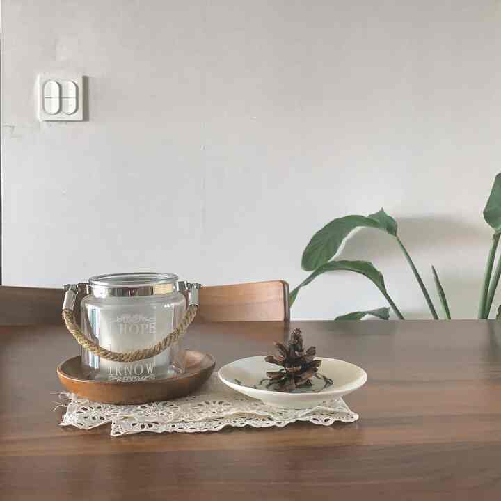 Natural wood tone dining table with lace placemat and decorative items, green plant on the right side in a clean kitchen space