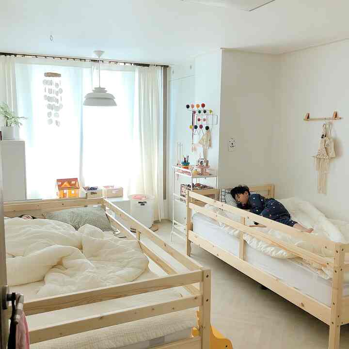 Bright white and wood-tone kids' room featuring two natural wood beds with children sleeping comfortably, creating a cozy atmosphere
