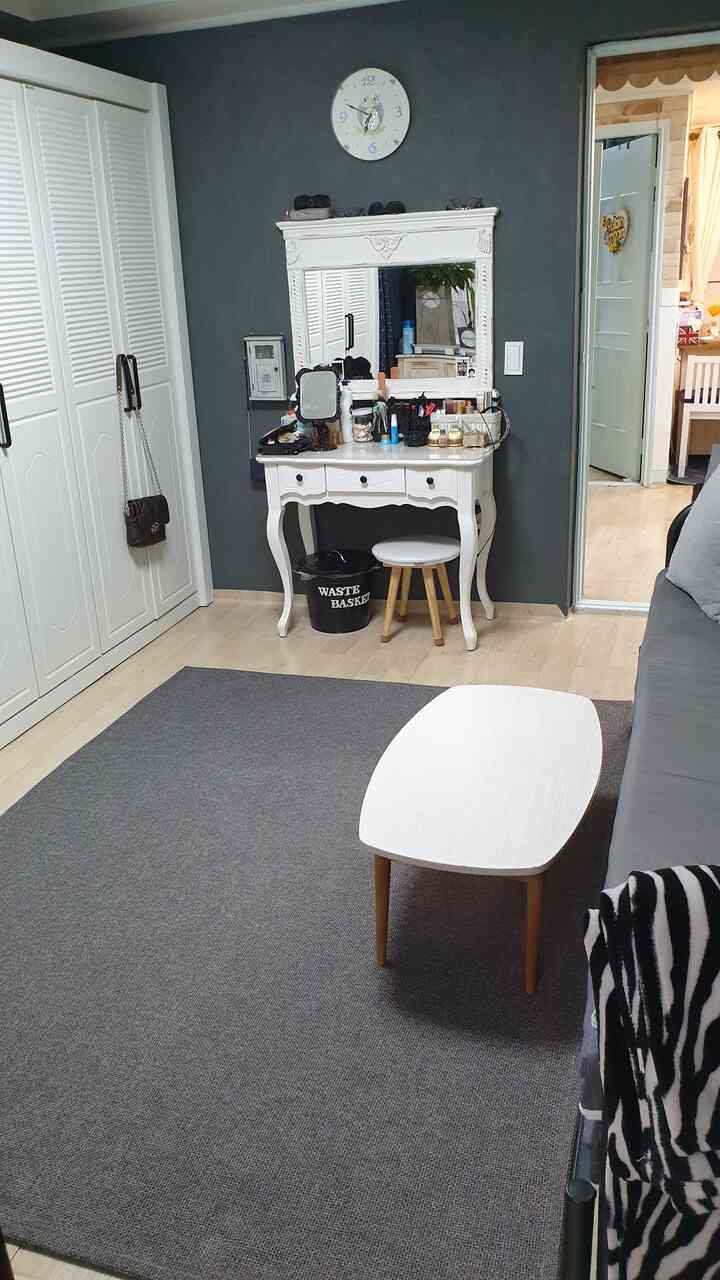 Compact bedroom in white and dark gray tones featuring an antique vanity and sofa bed with practical layout