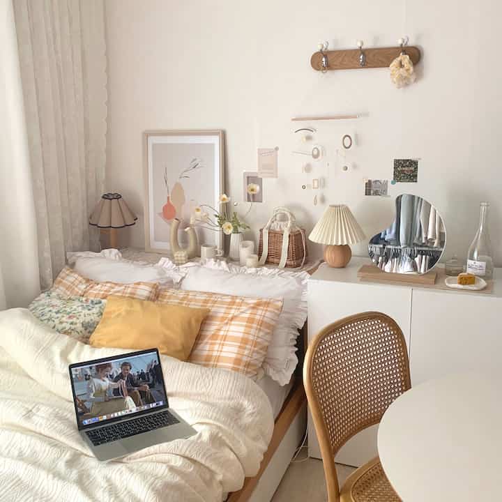 Natural toned studio bedroom featuring rattan chair, table lamp, and round mirror with cozy warm atmosphere