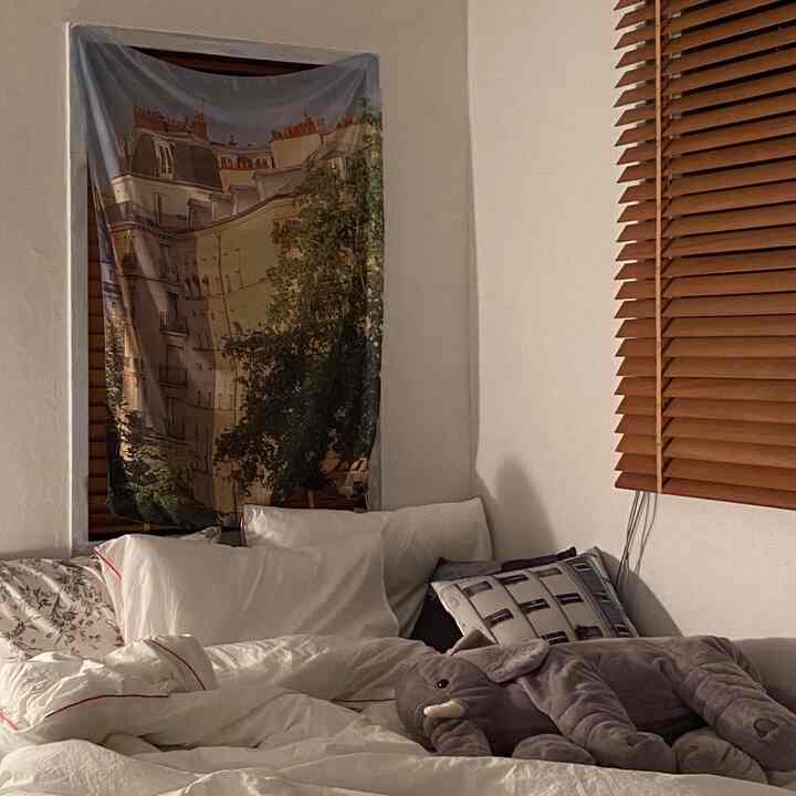 Cozy studio apartment bedroom featuring white bedding and warm wood-tone blinds with soft lighting