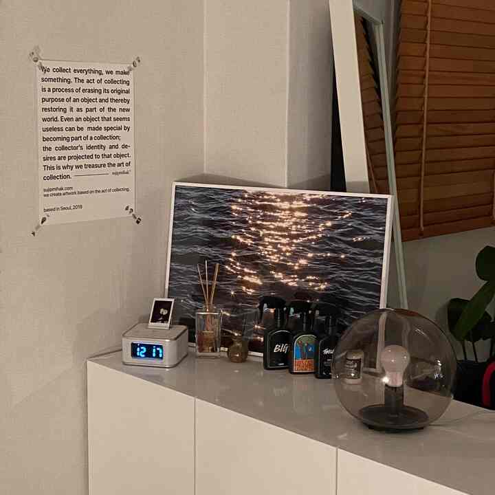 ホワイトトーンのリビングコーナー、白いキャビネットの上にテーブルランプと額縁、時計が配置されたシンプルな空間