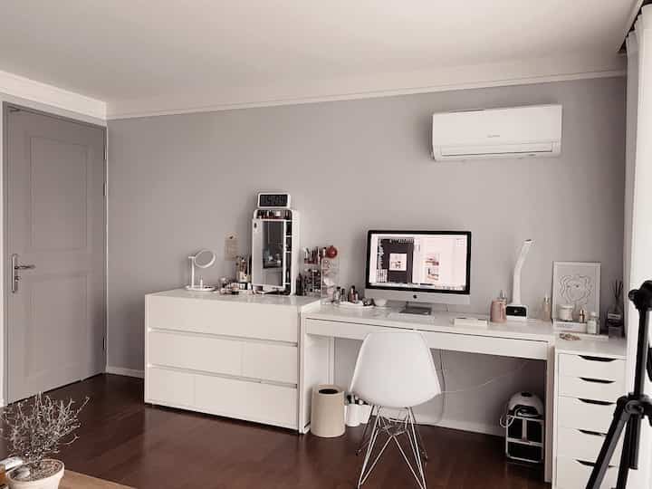 White and gray toned home office space featuring a clean desk, dresser, computer, and digital clock with a simple aesthetic