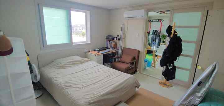 White and beige toned studio bedroom featuring bed, desk, and armchair in a compact layout