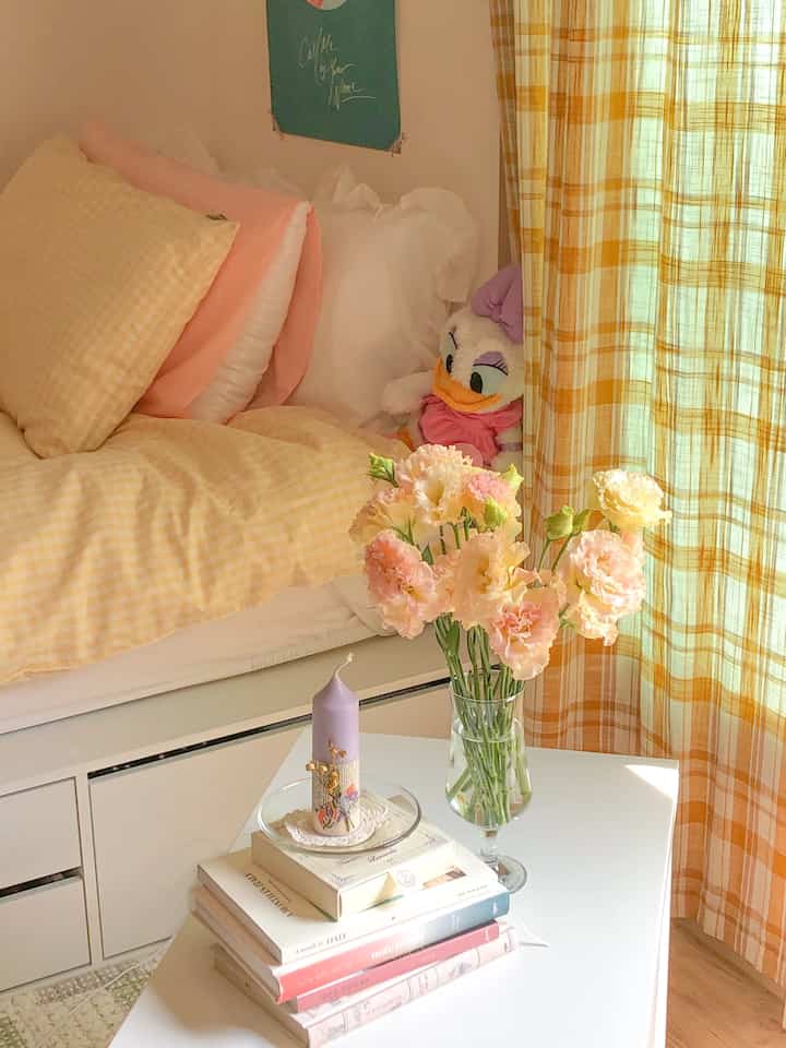 Yellow check and white tone bedroom featuring frilled pillows, a flower vase, and candle creating a cozy atmosphere