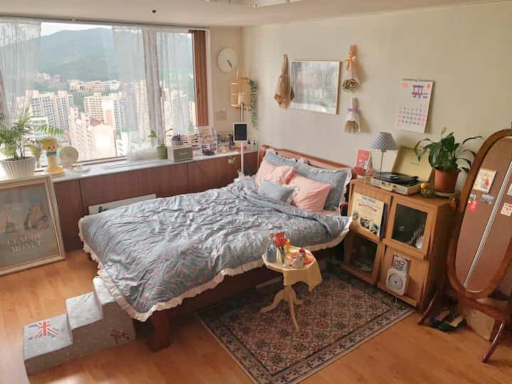 A vintage-style bedroom featuring natural wood tones and pastel blue bedding, accented by large windows and wooden furniture creating a cozy atmosphere