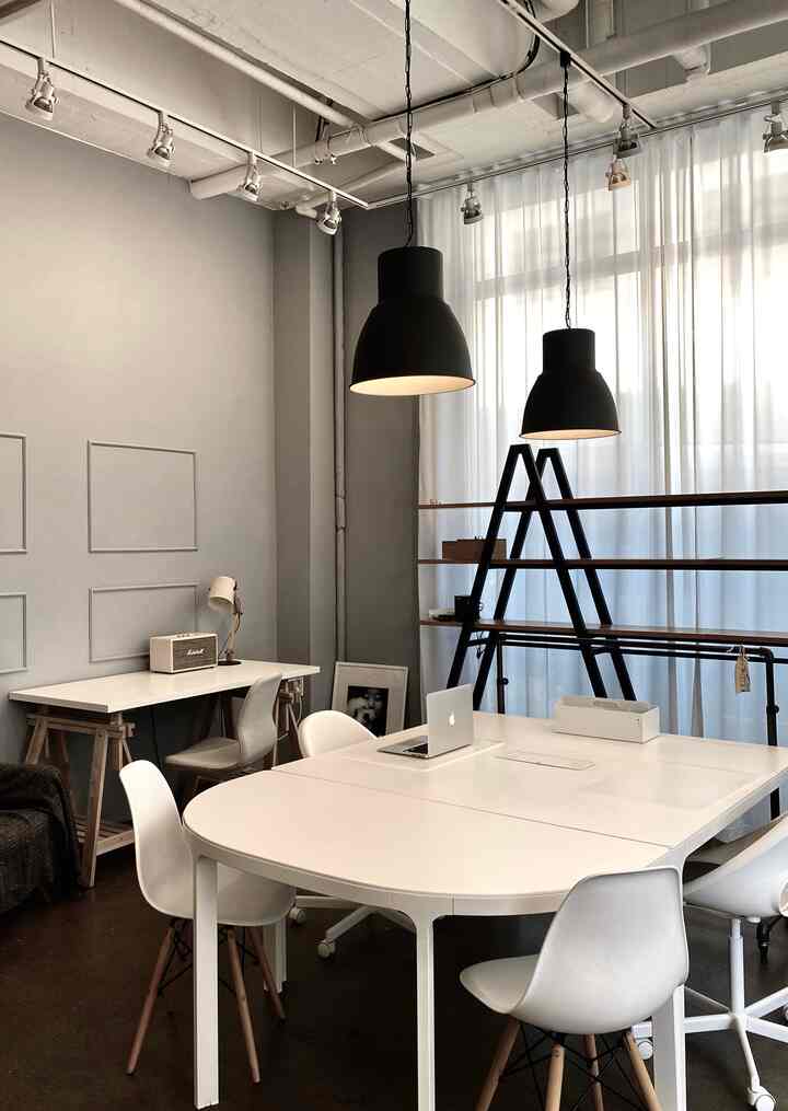 白とグレーのトーンのモダンなホームオフィス、白いテーブルと椅子が配置され、黒のペンダントライトが調和した雰囲気のあるインテリア