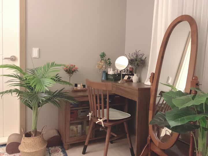 ブラウンの木目調と緑の植物が調和したナチュラルスタイルの小さな部屋、化粧台が配置された雰囲気のあるインテリア