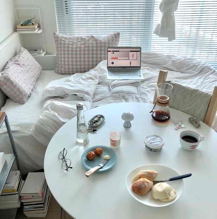 Compact bedroom in white and pink tones featuring a round dining table with home cafe elements, creating a cozy atmosphere