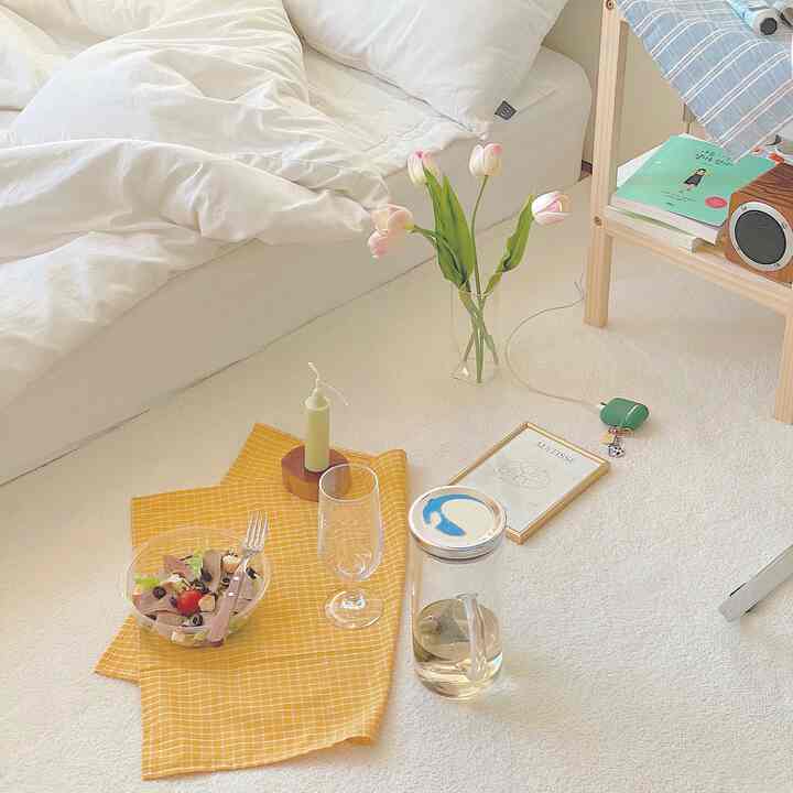 Natural modern white-toned bedroom with floor picnic setup including vase and framed art, creating a cozy atmosphere