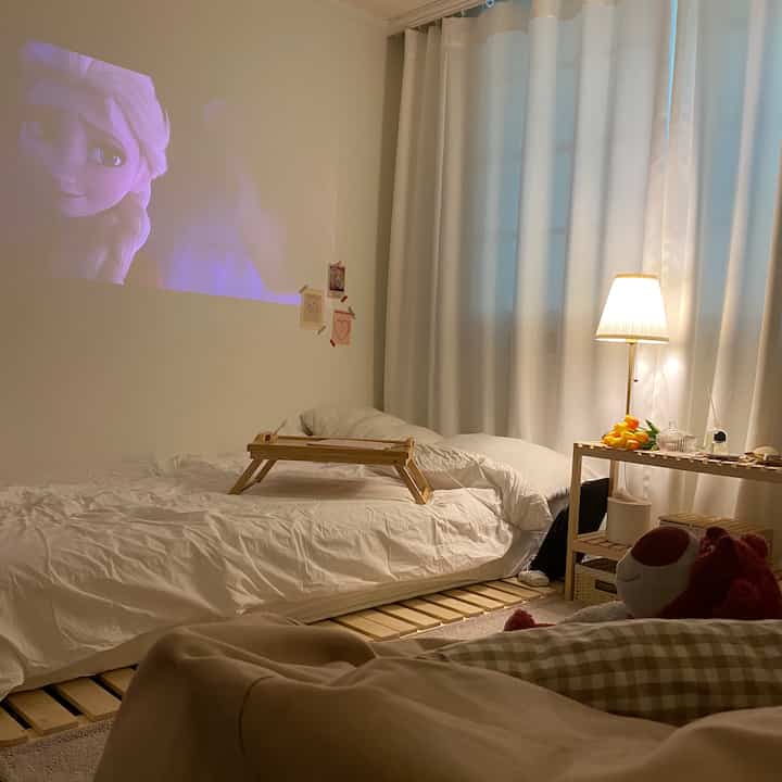 White and beige toned studio bedroom featuring a bed with wooden bed tray and warm lighting creating a cozy atmosphere