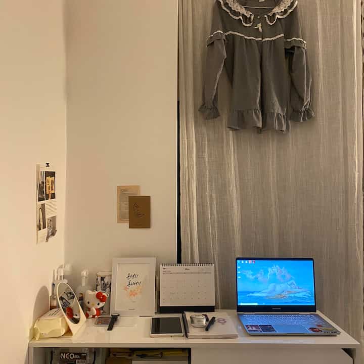 Beige and white toned bedroom home office featuring a clean desk with laptop and notebook, complemented by linen curtains for a cozy atmosphere