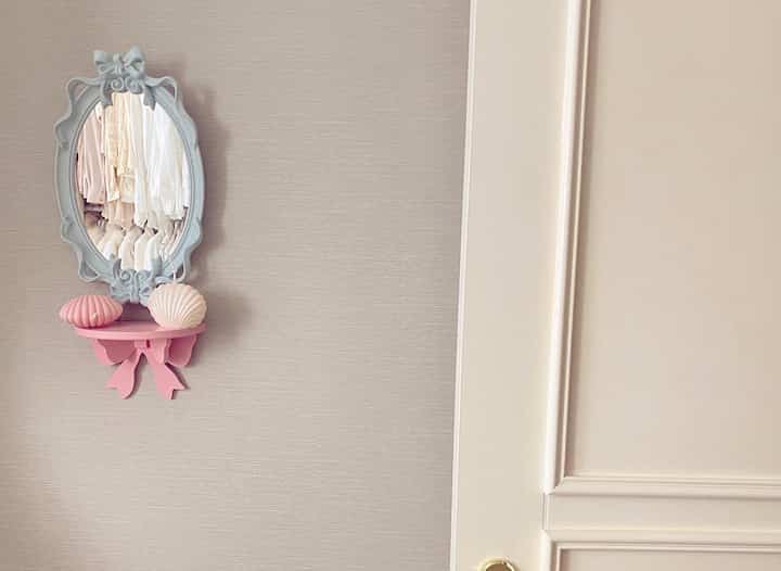 Pastel-toned wall featuring a pink shelf with decorative elements and an ornate French Country style mirror