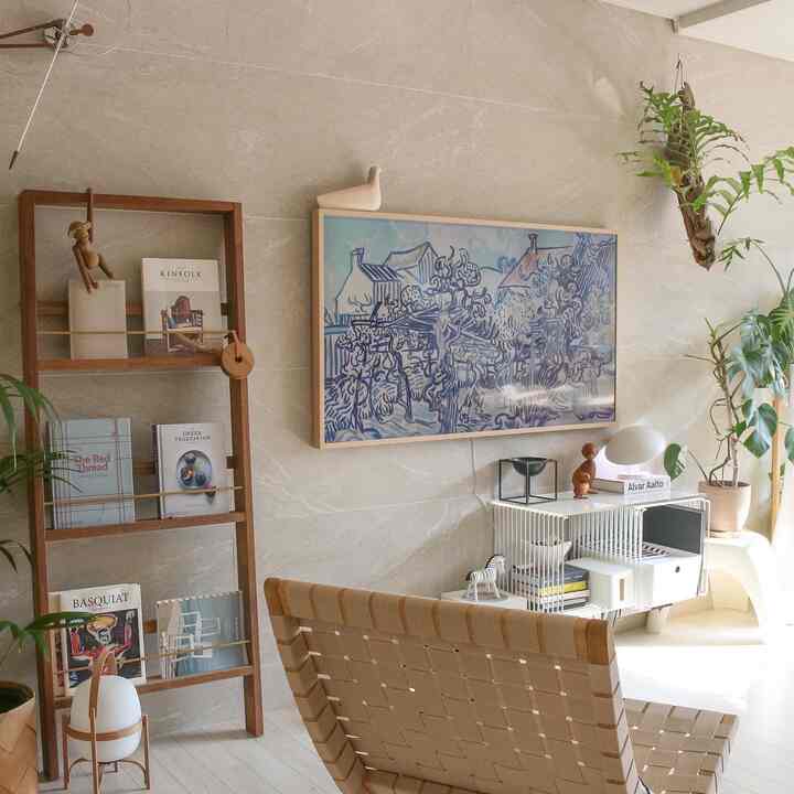 Natural and cozy living room in beige and wood tones featuring wooden bookshelf, art TV, and plants