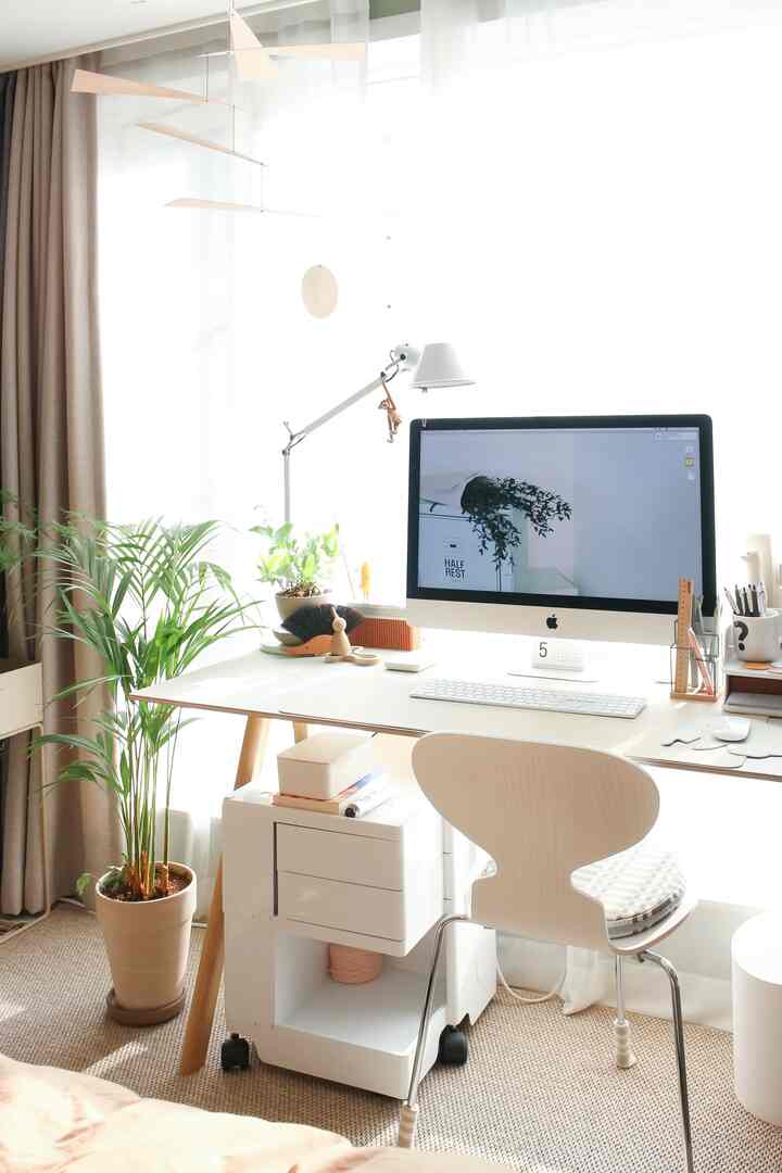 Bright white-tone home office workspace featuring a white desk, chair, computer, and green plants in a clean setting