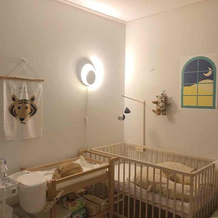 White and wood-toned baby room featuring a crib, changing table, and a cat resting, creating a warm atmosphere