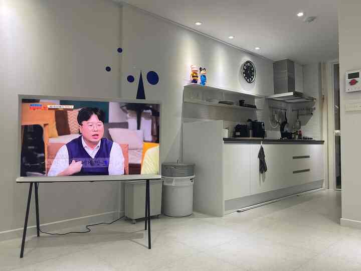Modern living room and kitchen space in white tones featuring a TV stand and kitchen hood with simple interior design