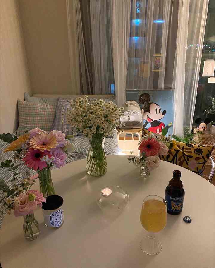 白を基調とした寝室空間、花瓶とカーテン、キャンドルが置かれたコンパクトなテーブルが落ち着いた雰囲気を演出するインテリア