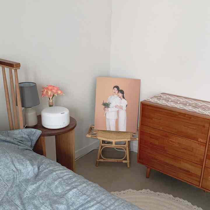 Vintage bedroom corner featuring white walls, wood-tone chest of drawers, and a rattan stool