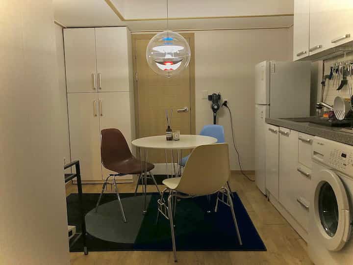 White and brown toned compact kitchen dining area featuring a round dining table with multicolor chairs in a neat setting