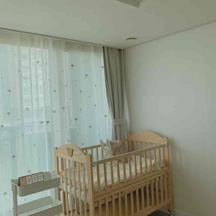 ナチュラルなベージュ色調の赤ちゃん部屋、木製ベビーベッドと刺繍カーテンが配置された、落ち着いた清潔な雰囲気のインテリア