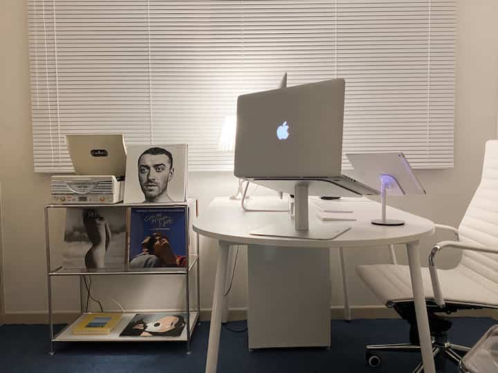 White and blue toned home office featuring a white desk and chair, metal modular shelves with LPs and a turntable in a clean workspace